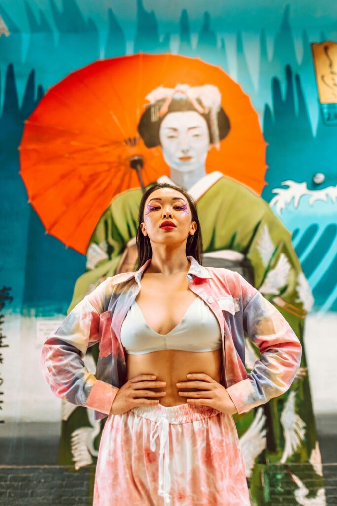 pexels-photo-6785041-6785041 A woman poses stylishly in front of a vibrant geisha mural blending tradition and modernity.
